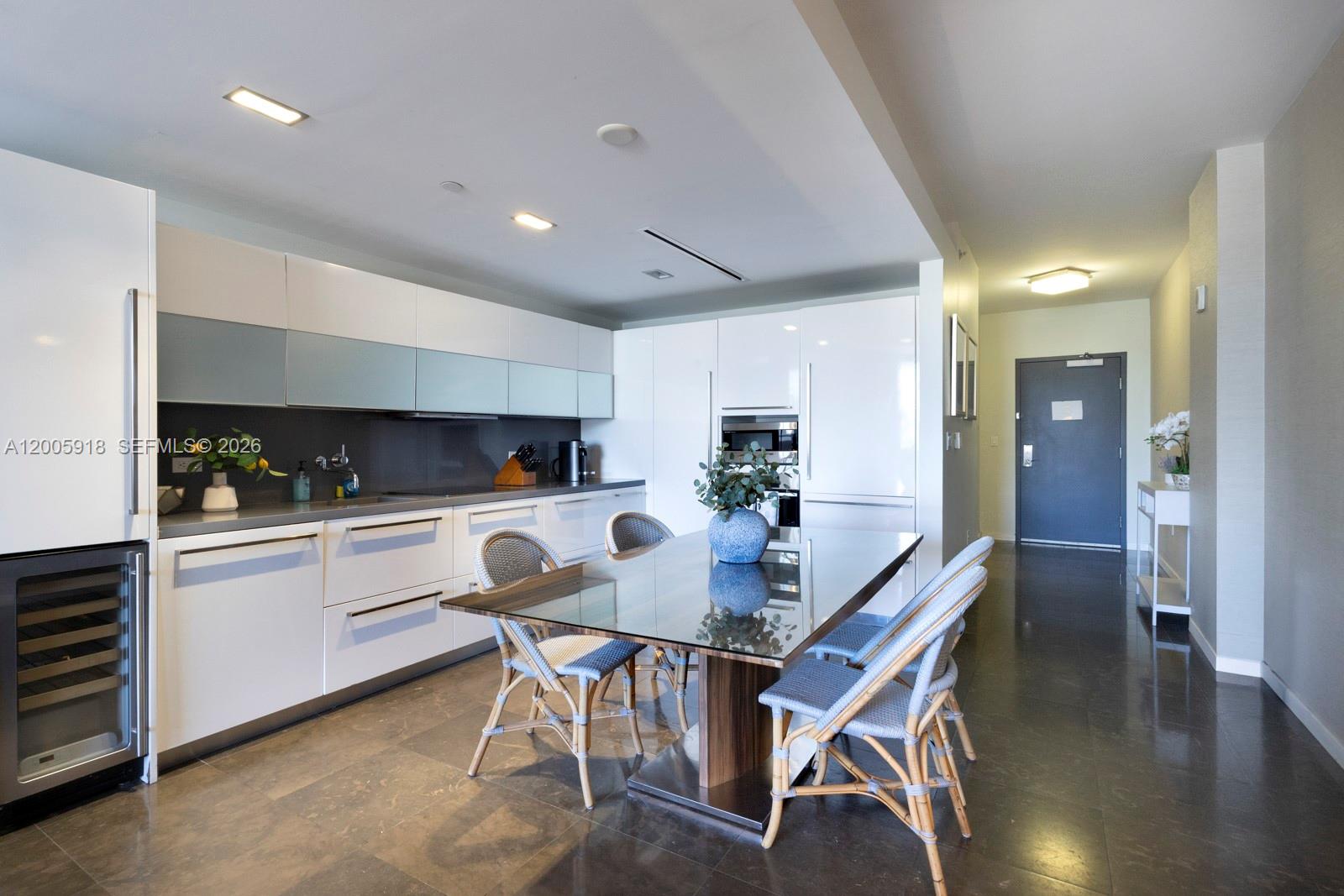 A modern kitchen features white cabinetry, a glass-topped dining table, and dark tile flooring — 220 21st St # 303, Miami Beach FL 33139, MIAMI BEACH, FL