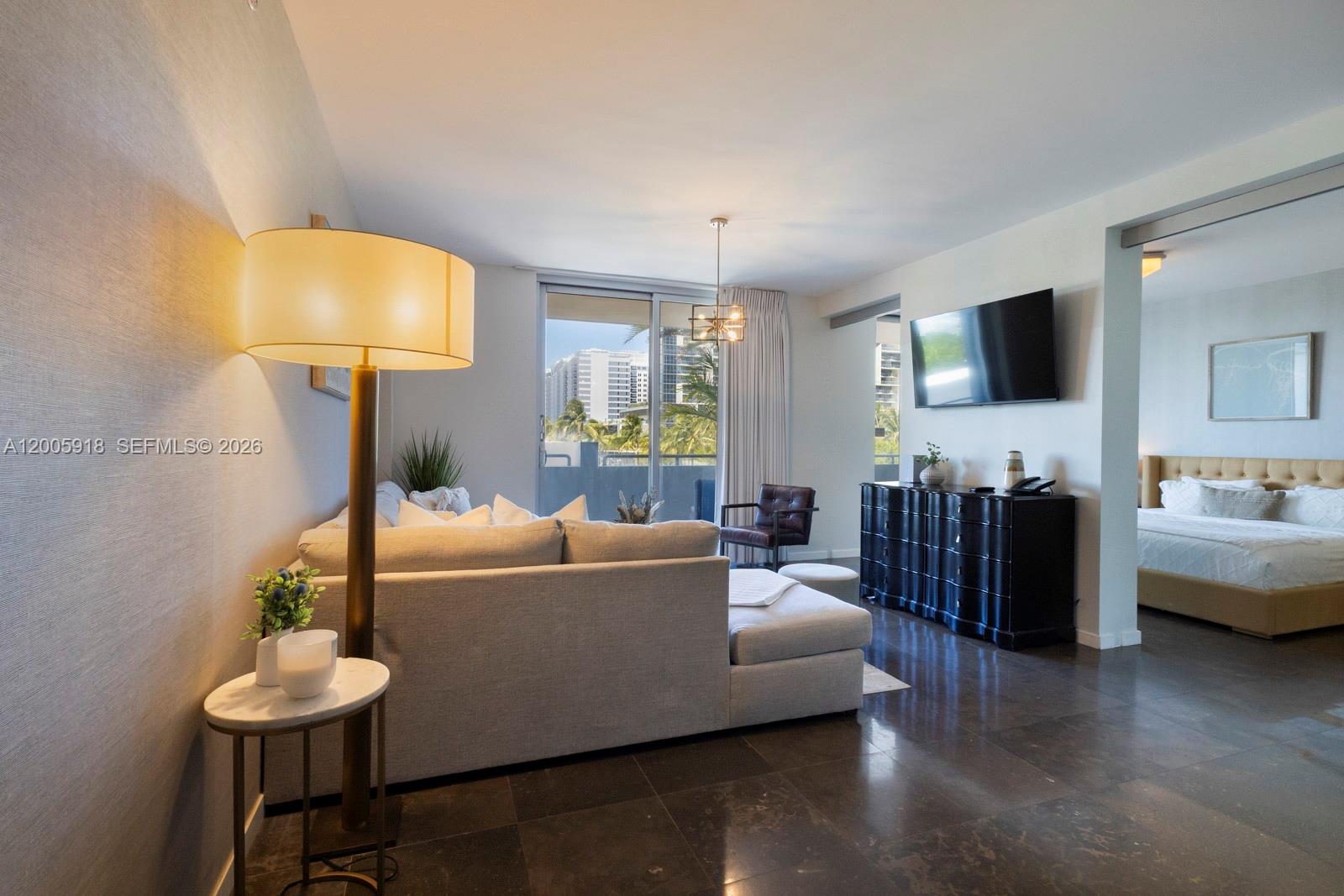 A living room with a sectional sofa, floor lamp, and adjacent bedroom with tiled floors — 220 21st St # 303, Miami Beach FL 33139, MIAMI BEACH, FL