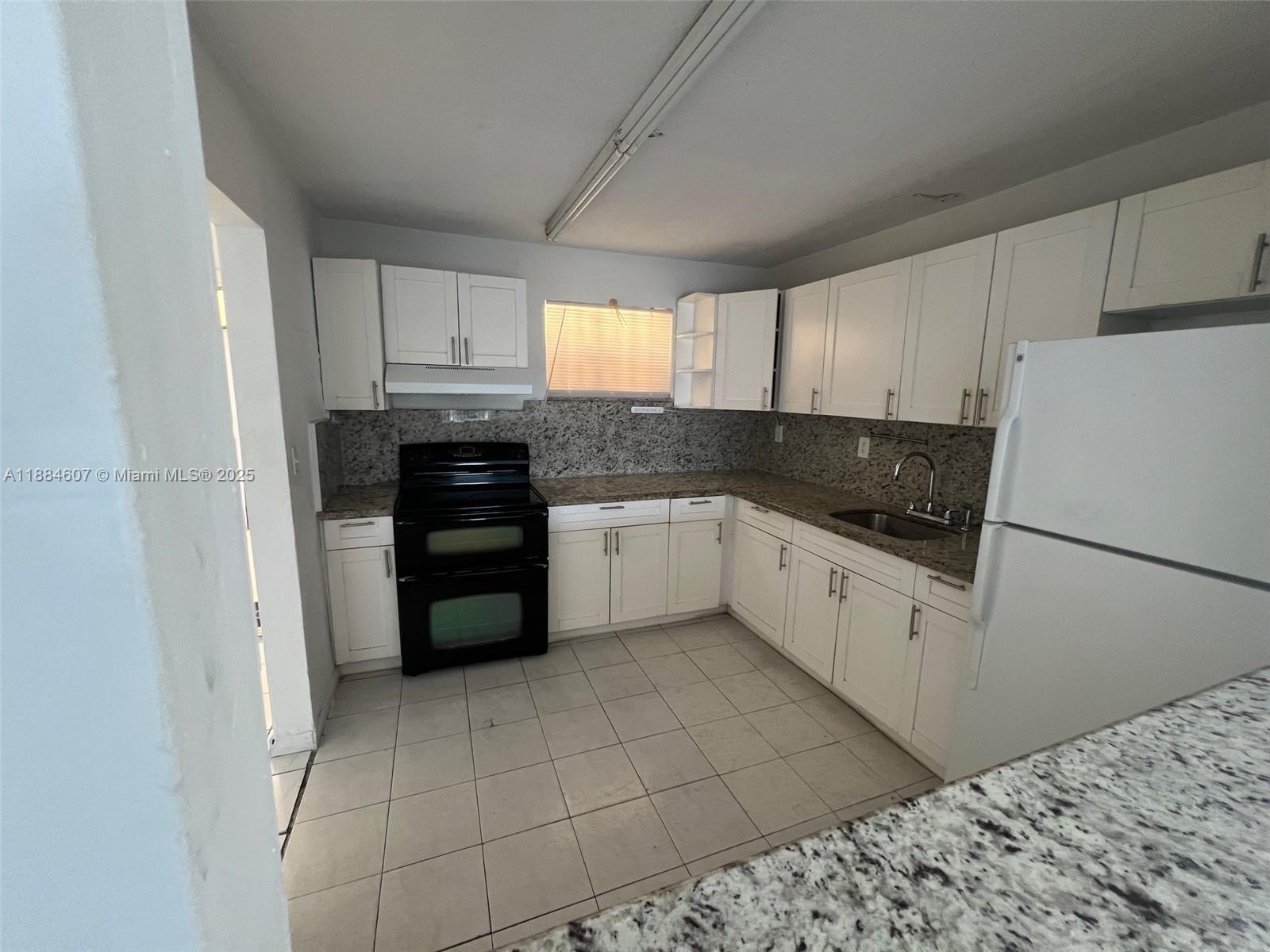 A kitchen features white cabinets, granite countertops, a black stove, and light-colored tile flooring — 887 W 29th St # 1, Hialeah FL 33012, HIALEAH, FL