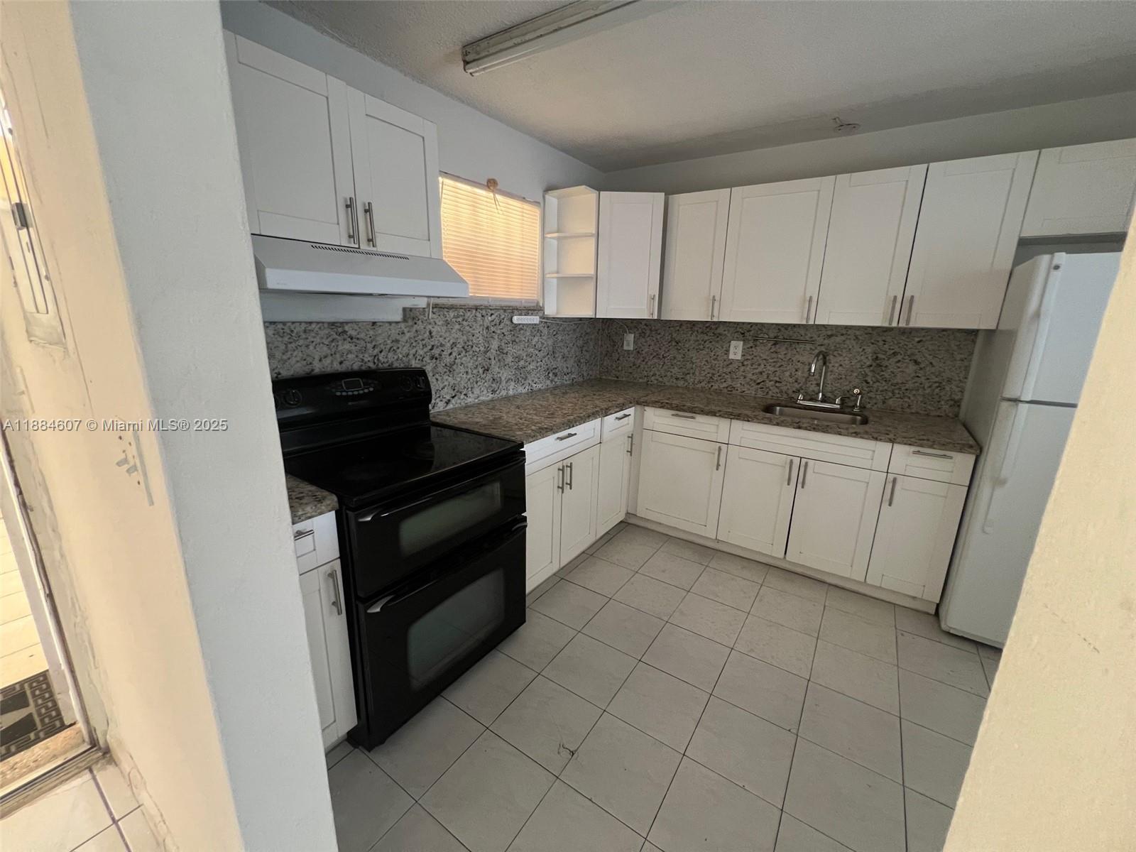 A kitchen features white cabinets, granite countertops, a black stove, and light-colored floor tiles — 887 W 29th St # 1, Hialeah FL 33012, HIALEAH, FL
