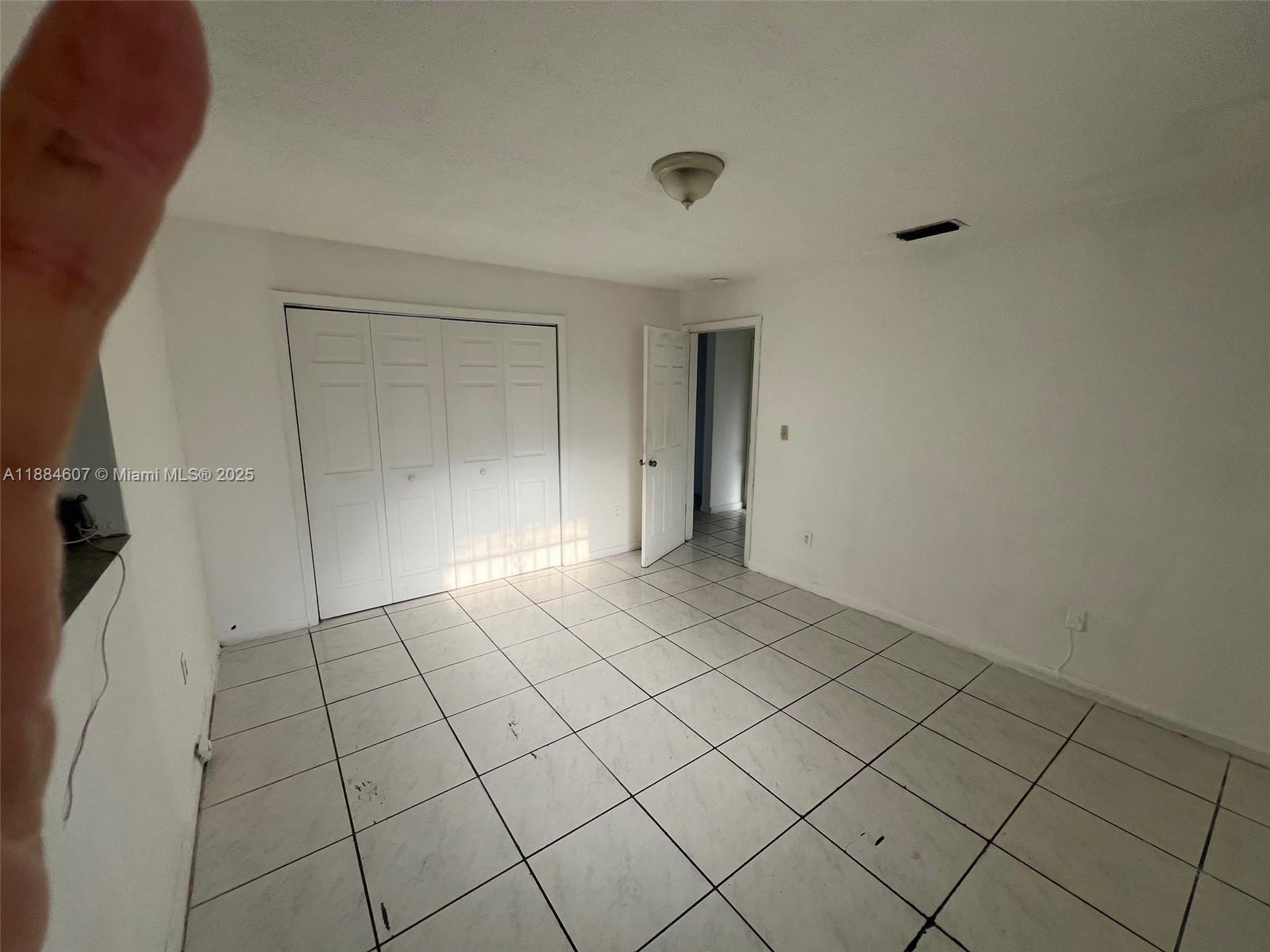 A bedroom with white walls, white tile flooring, a closet, and an open doorway — 887 W 29th St # 1, Hialeah FL 33012, HIALEAH, FL