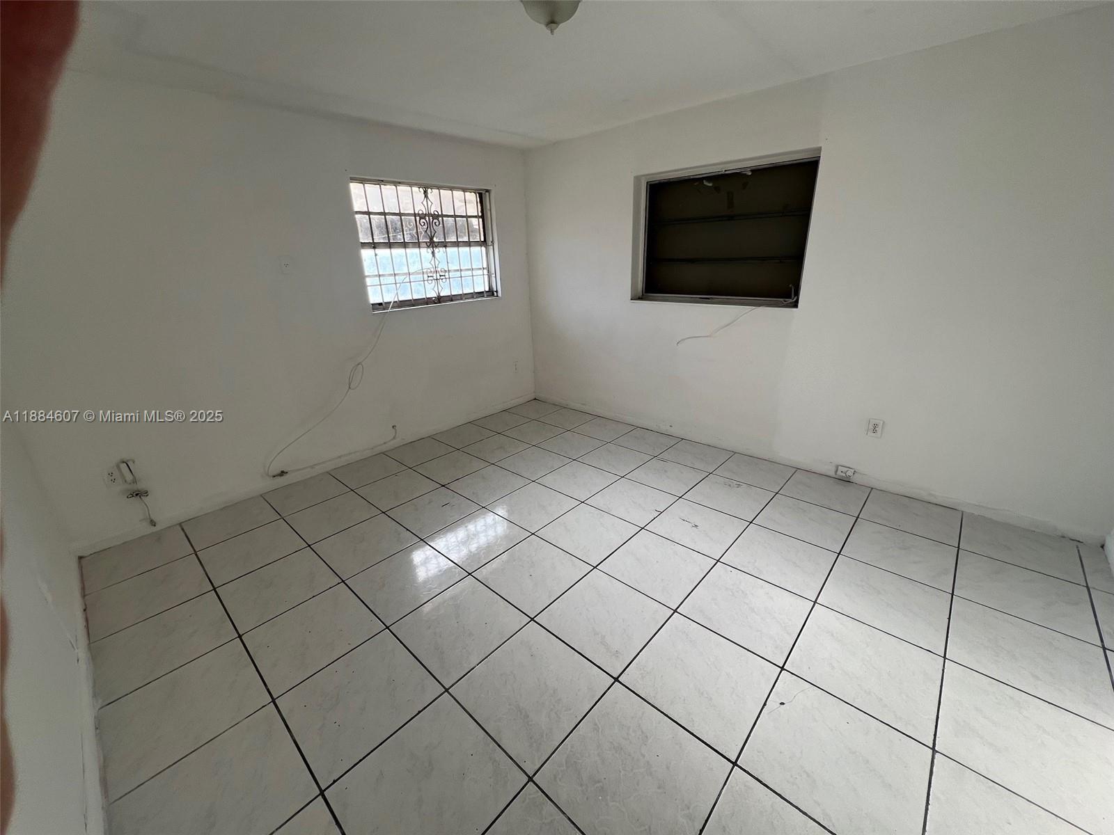 An empty room features white walls, light-colored square floor tiles, and two windows — 887 W 29th St # 1, Hialeah FL 33012, HIALEAH, FL