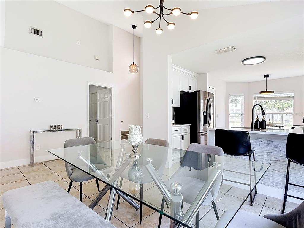 A dining area with a glass table and chairs sits adjacent to a modern kitchen — 1021 TOURMALINE DRIVE, KISSIMMEE, FL