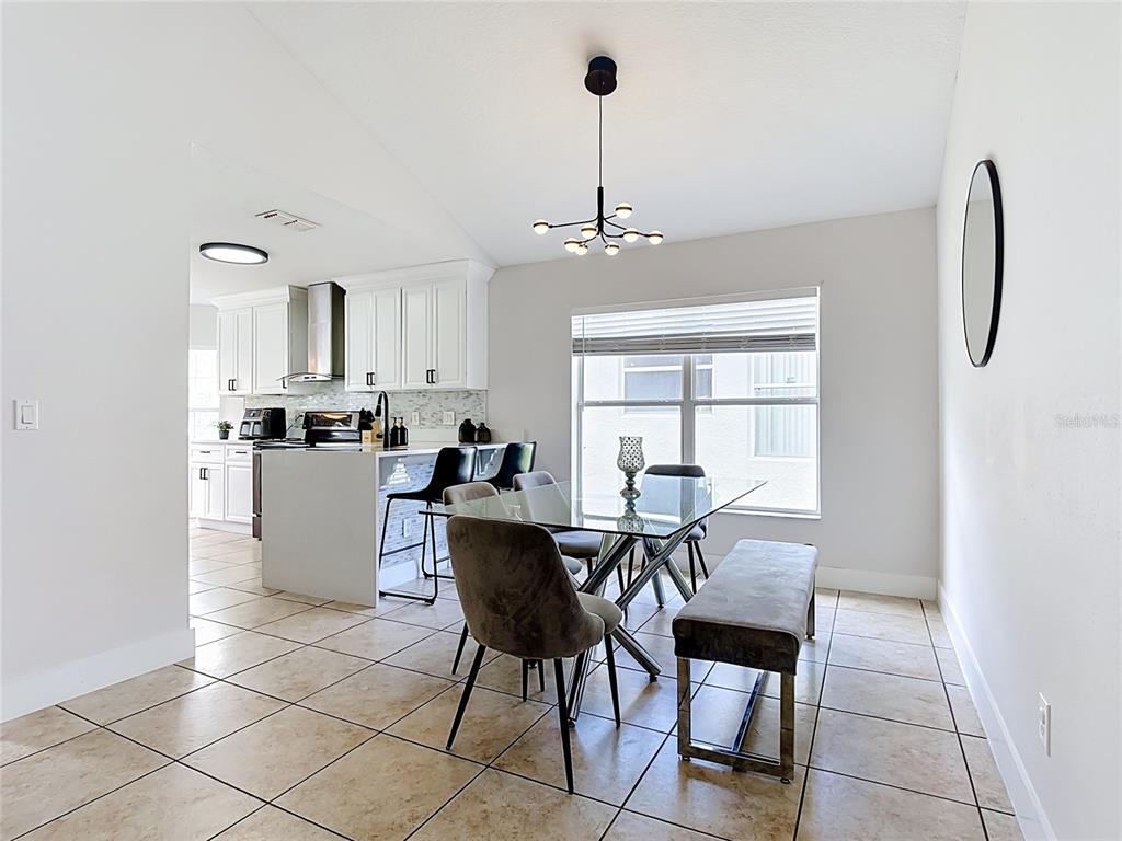 A dining area with a glass table and bench sits adjacent to a white kitchen — 1021 TOURMALINE DRIVE, KISSIMMEE, FL