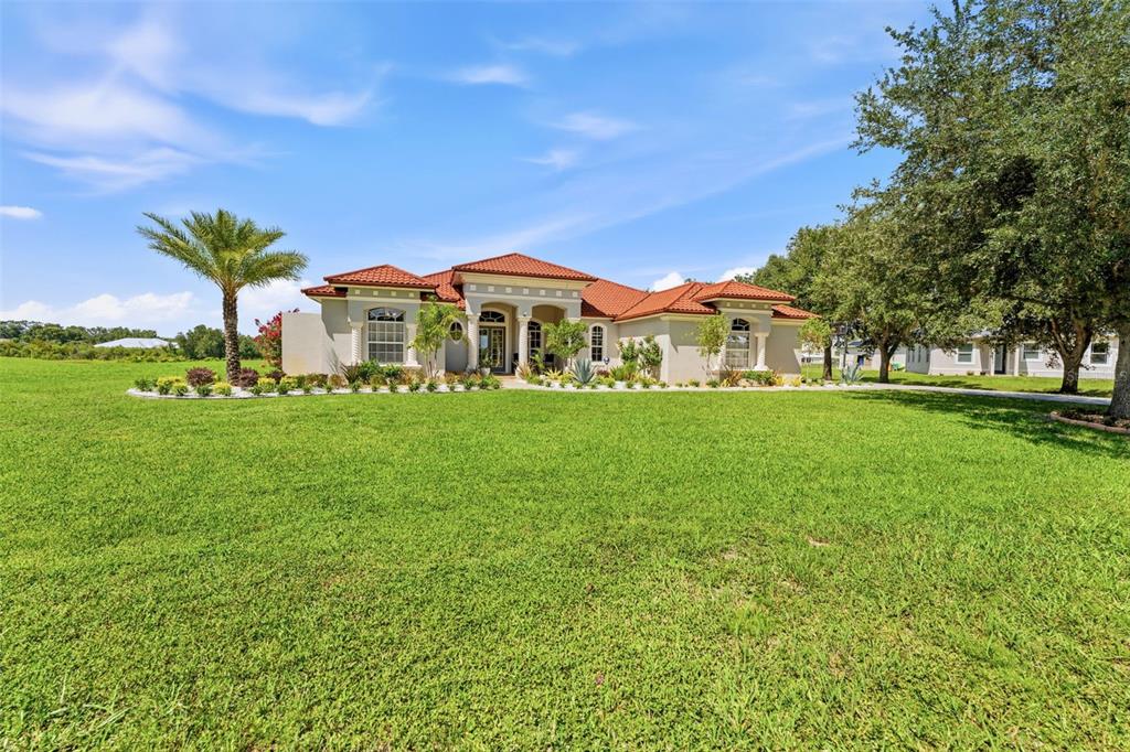 A single-story house with a red tile roof sits behind a large, grassy front lawn — 24355 HIDEOUT TRAIL, LAND O LAKES, FL