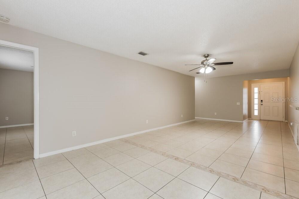 An empty living room with beige tile floors, neutral walls, and a ceiling fan — 12438 DAWN VISTA DRIVE, RIVERVIEW, FL