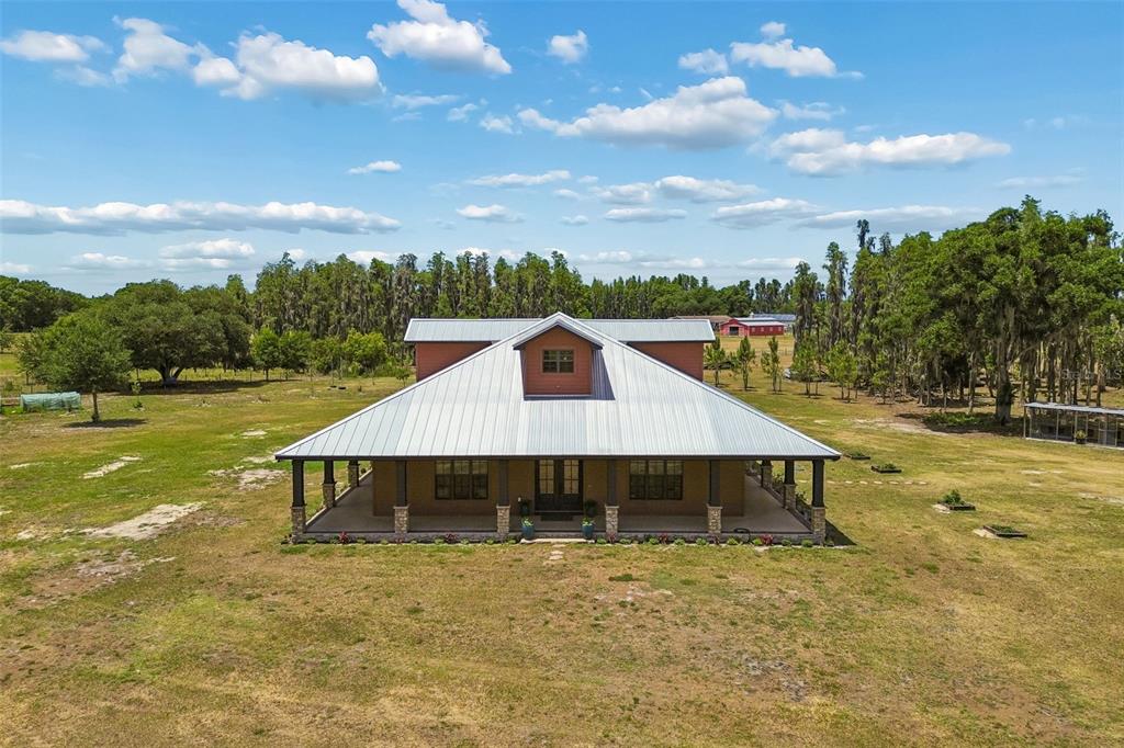 An aerial view of a single-story house with a metal roof and a wrap-around porch — 41451 NIPPER ROAD, ZEPHYRHILLS, FL