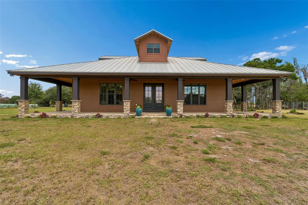 A single-story house with a metal roof, stone-based columns, and a central dormer window — 41451 NIPPER ROAD, ZEPHYRHILLS, FL