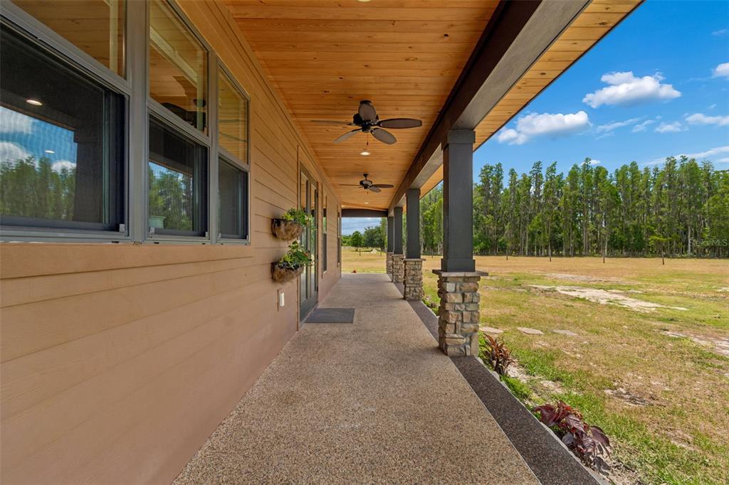 A covered porch with a wood ceiling, ceiling fans, and stone-based columns overlooks a grassy field — 41451 NIPPER ROAD, ZEPHYRHILLS, FL