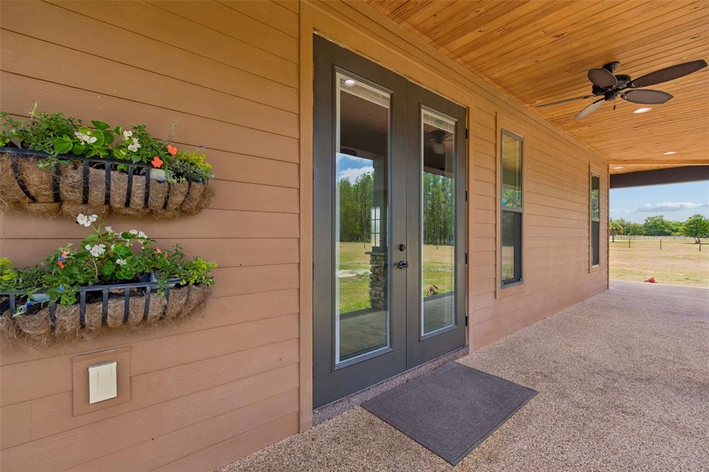 A covered porch features tan siding, double glass doors, and two wall-mounted flower planters — 41451 NIPPER ROAD, ZEPHYRHILLS, FL