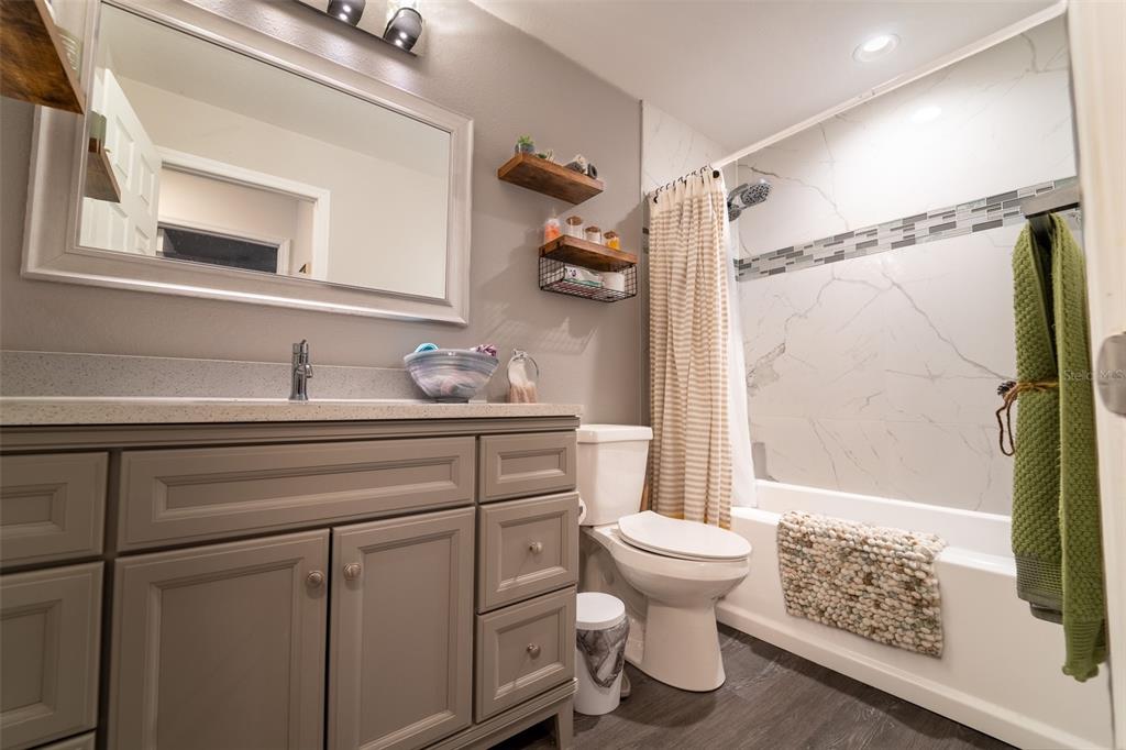 A bathroom features a gray vanity, a toilet, and a tub-shower combo with marble-look tile — 7407 MOUNT VERNON ROAD, TAMPA, FL