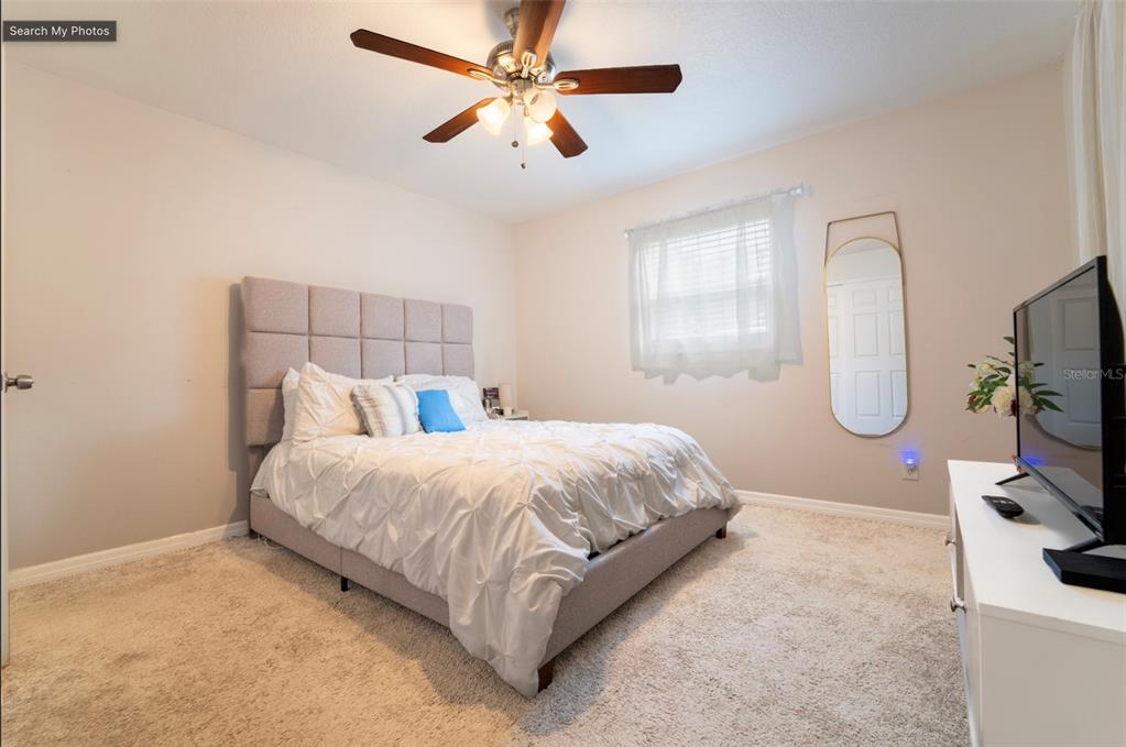 A bedroom features a tufted gray bed, white bedding, a ceiling fan, and a mirror — 7407 MOUNT VERNON ROAD, TAMPA, FL