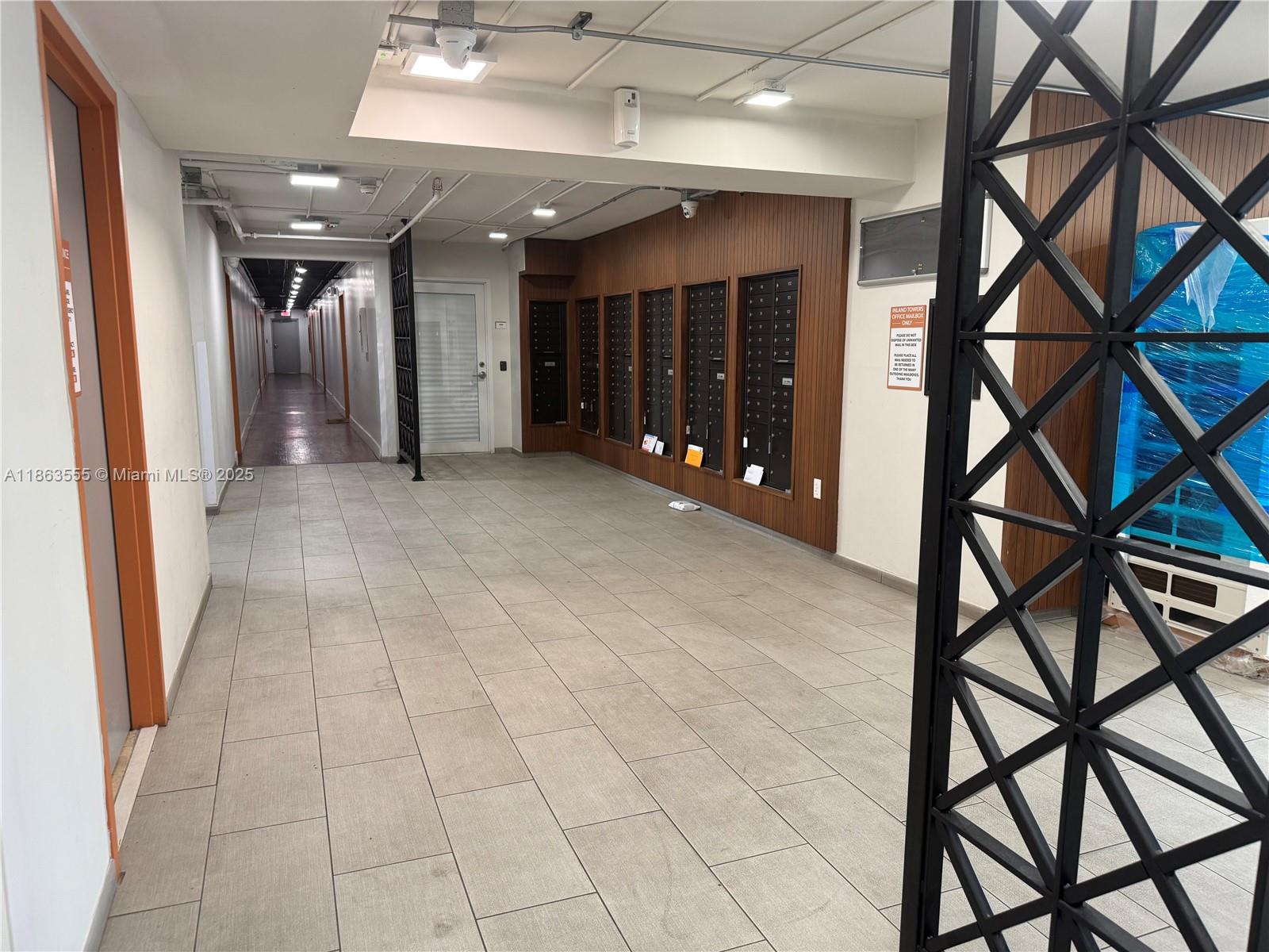 This indoor hallway features a wall of mailboxes, tiled flooring, and a decorative metal screen — 2075 NE 164th St # 105, North Miami Beach FL 33162, NORTH MIAMI BEACH, FL