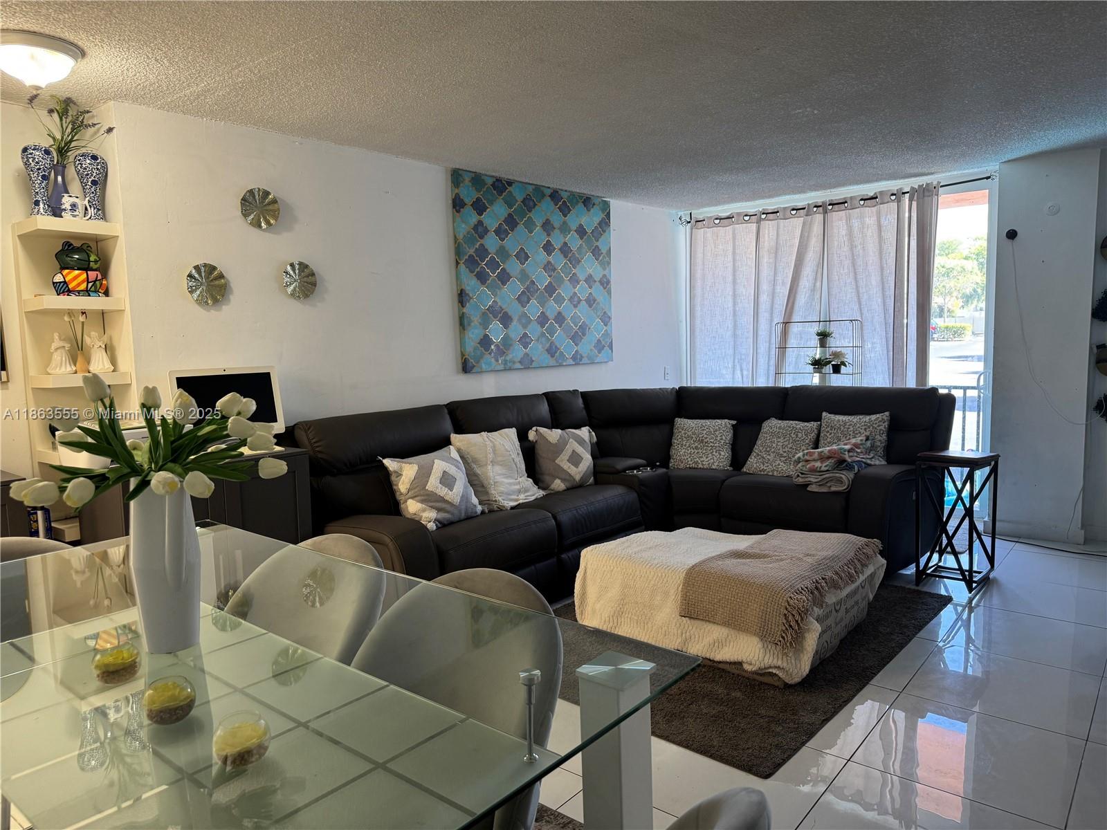A living room features a dark sectional sofa, a glass dining table, and tiled floors — 2075 NE 164th St # 105, North Miami Beach FL 33162, NORTH MIAMI BEACH, FL