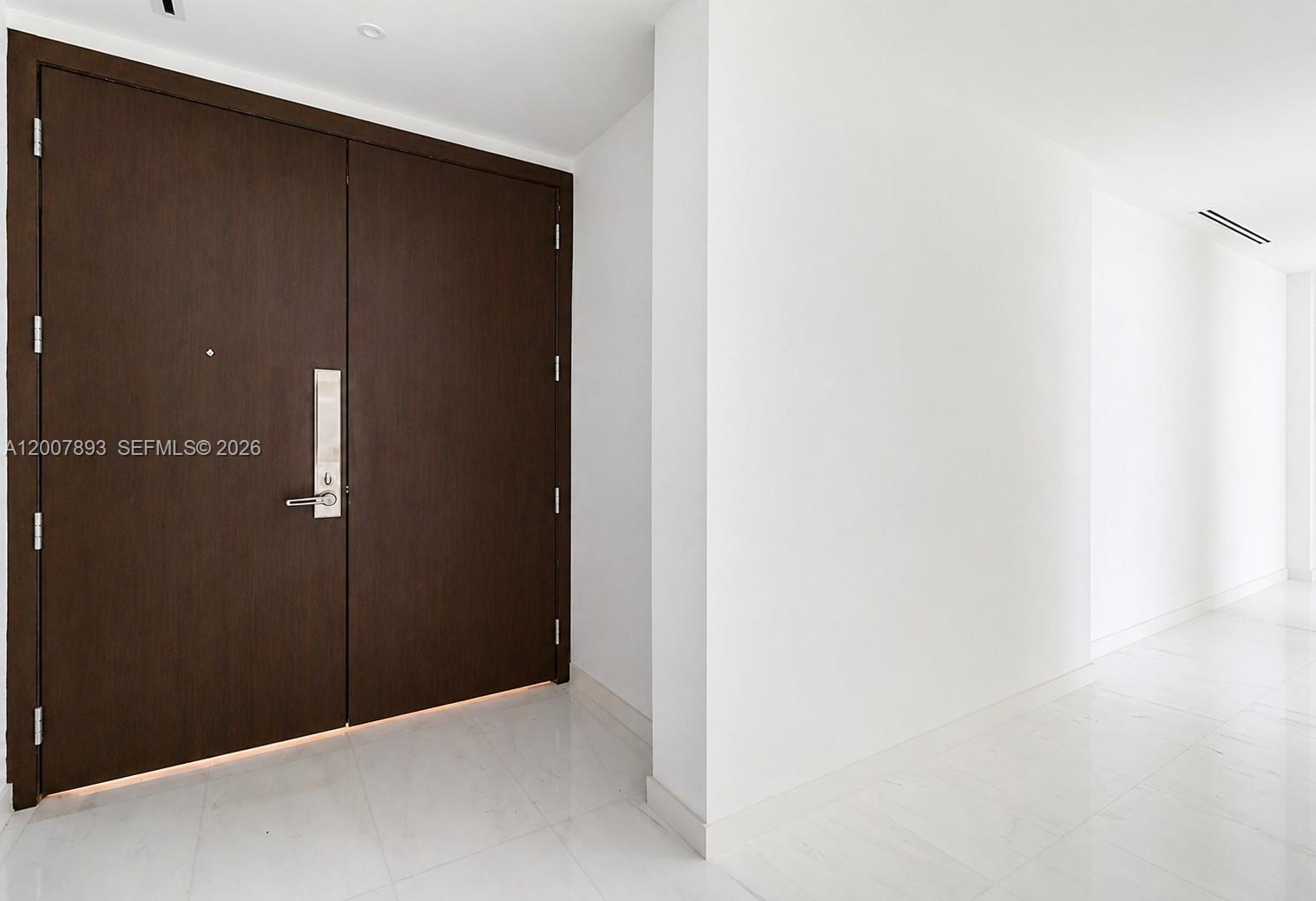 A dark wood double door stands in a white hallway with light marble flooring — 300 Biscayne Boulevard Way # 4201E, Miami FL 33131, MIAMI, FL