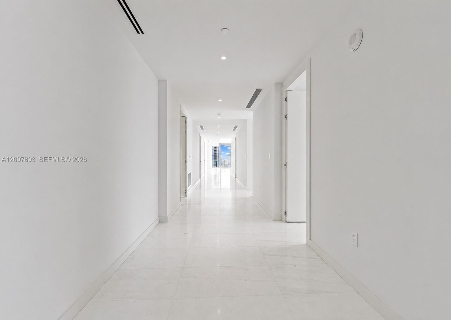 A long, white hallway features polished tile flooring, recessed lighting, and multiple doorways — 300 Biscayne Boulevard Way # 4201E, Miami FL 33131, MIAMI, FL