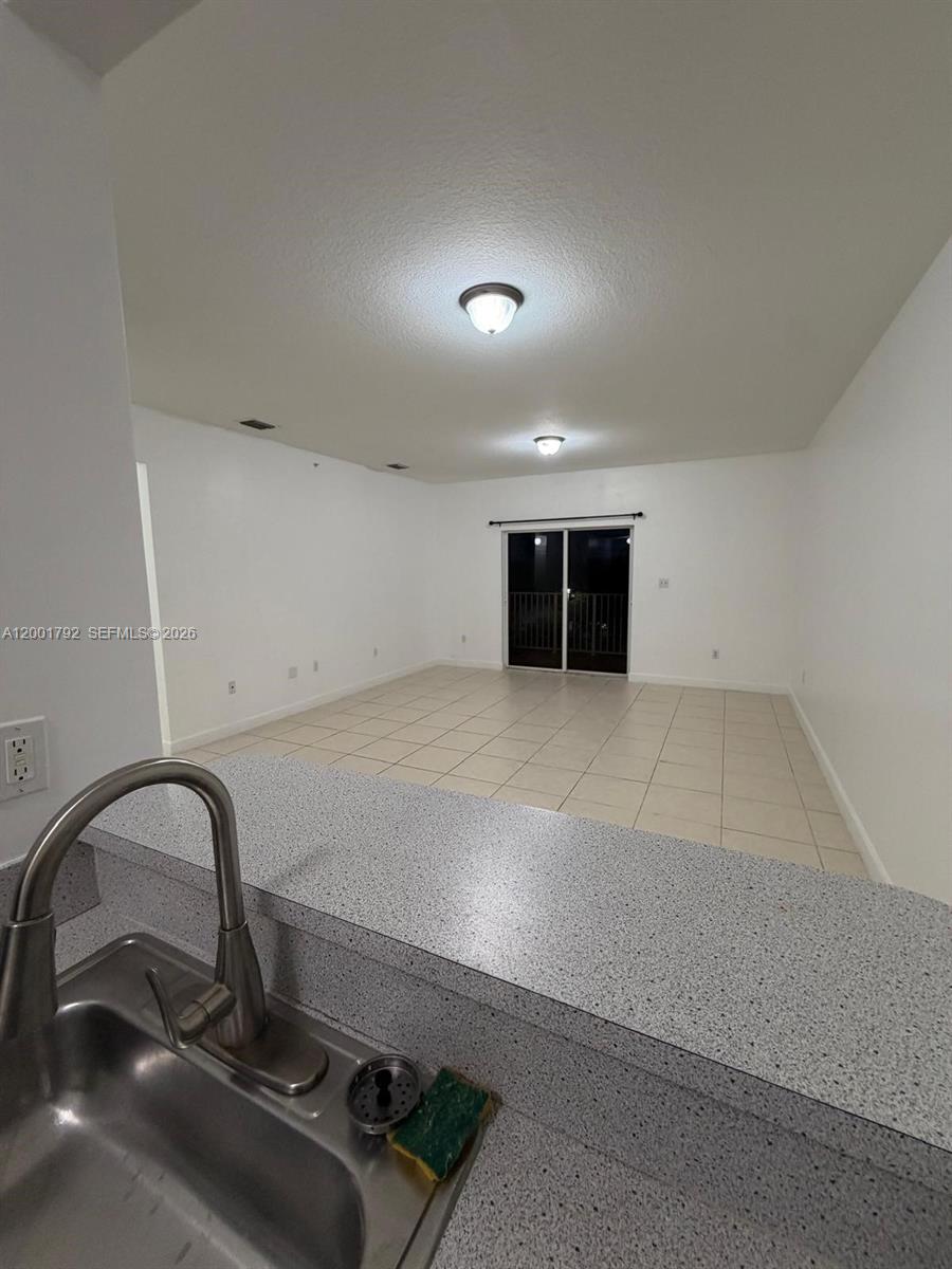 A kitchen sink with a speckled countertop overlooks an empty living area with tile flooring — 1300 NE 109th St # 404, Miami FL 33161, MIAMI, FL