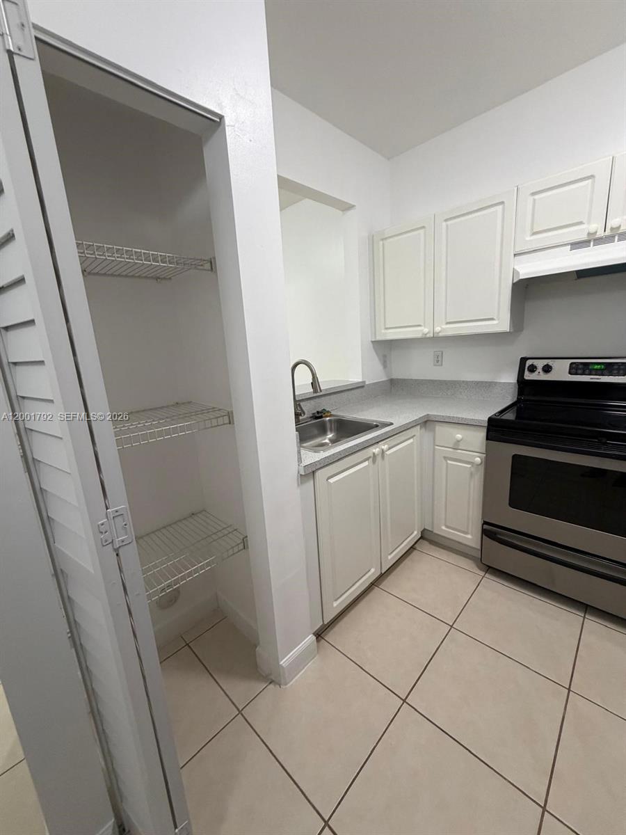 A kitchen features white cabinets, stainless steel appliances, a pantry, and light-colored tile flooring — 1300 NE 109th St # 404, Miami FL 33161, MIAMI, FL