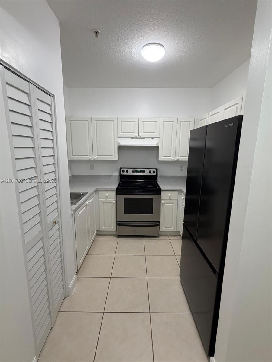 A galley-style kitchen features white cabinets, stainless steel appliances, and light-colored floor tiles — 1300 NE 109th St # 404, Miami FL 33161, MIAMI, FL
