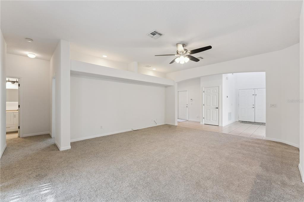 A spacious living room features beige carpeting, a ceiling fan, and a large recessed wall — 5295 ADAIR OAK DRIVE, ORLANDO, FL