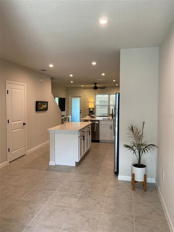 A kitchen with a white island, light tile flooring, and recessed lighting opens to a living area — 12245 GRIZZLY LANE, NEW PORT RICHEY, FL