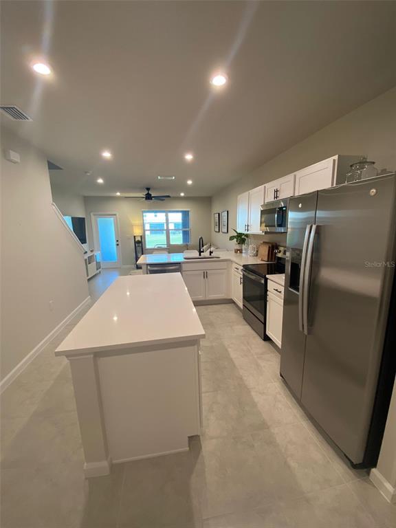 A modern kitchen features a white island, stainless steel appliances, and light-colored tile flooring — 12245 GRIZZLY LANE, NEW PORT RICHEY, FL