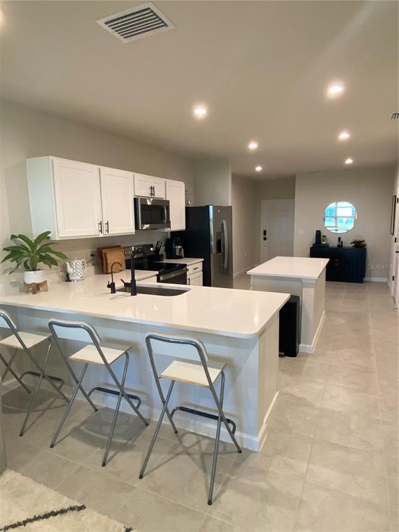 A kitchen features white cabinets, quartz countertops, a breakfast bar with stools, and stainless appliances — 12245 GRIZZLY LANE, NEW PORT RICHEY, FL
