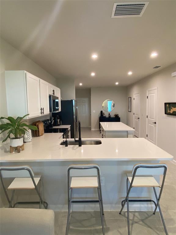 A kitchen features white cabinets, a quartz island, and a breakfast bar with three stools — 12245 GRIZZLY LANE, NEW PORT RICHEY, FL