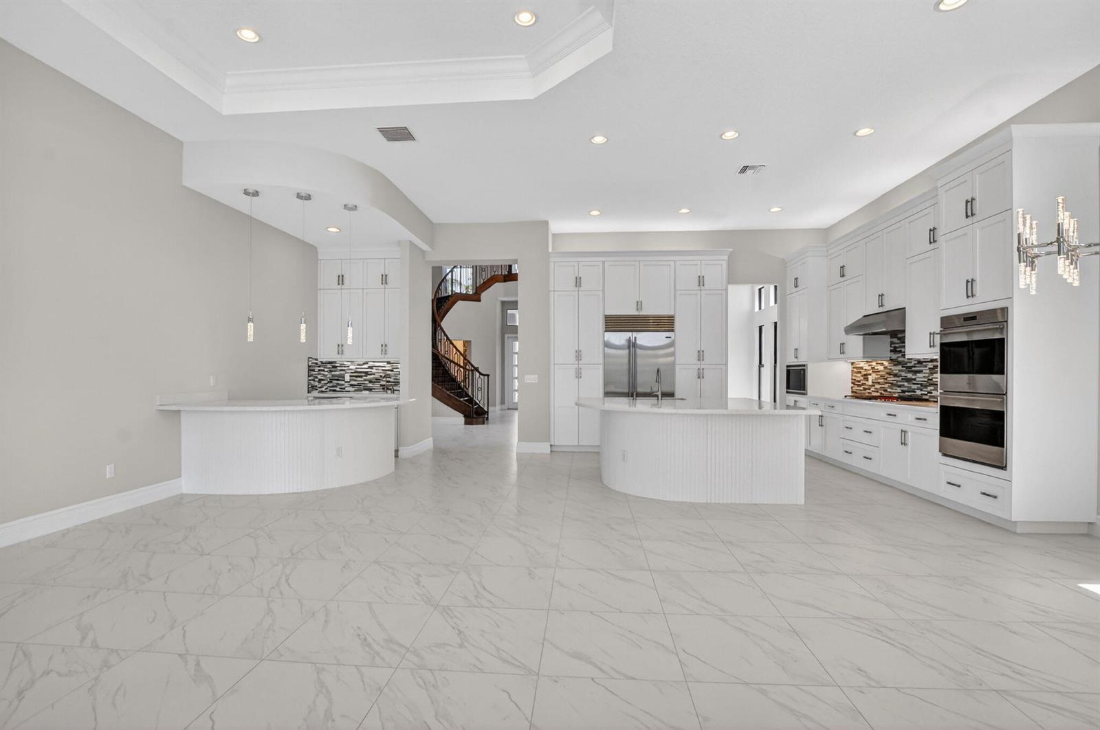 A spacious white kitchen with marble-look tile floors, curved islands, and a view of a staircase — 9168 Benedetta Place, Boca Raton FL 33496, BOCA RATON, FL