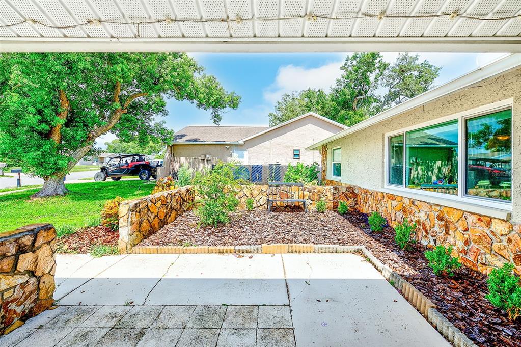 A stone-walled patio area sits beside a house with a concrete slab and mulch landscaping — 8741 HONEYCOMB DRIVE, PORT RICHEY, FL