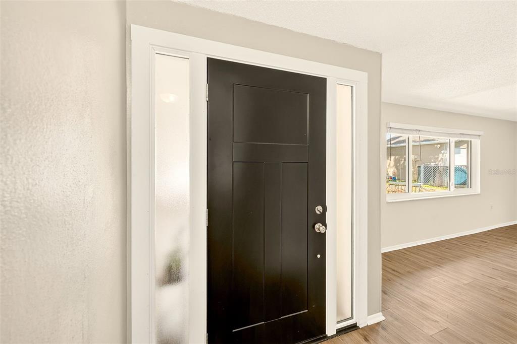 A black front door with side windows opens into a room with light-colored walls — 8741 HONEYCOMB DRIVE, PORT RICHEY, FL
