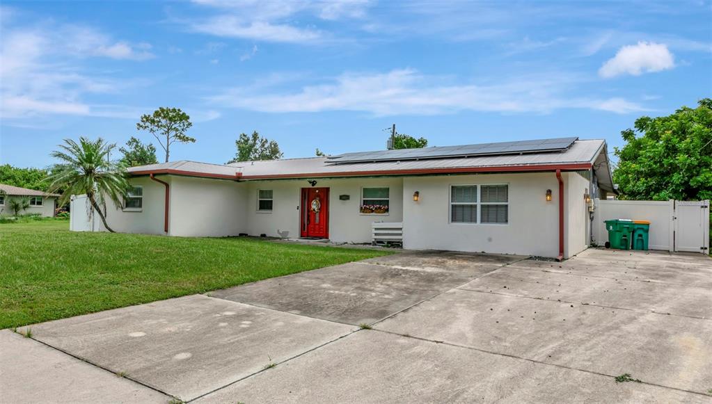 A single-story house with a white exterior, red front door, and solar panels on the roof — 509 RIDGEWOOD STREET NW, PORT CHARLOTTE, FL