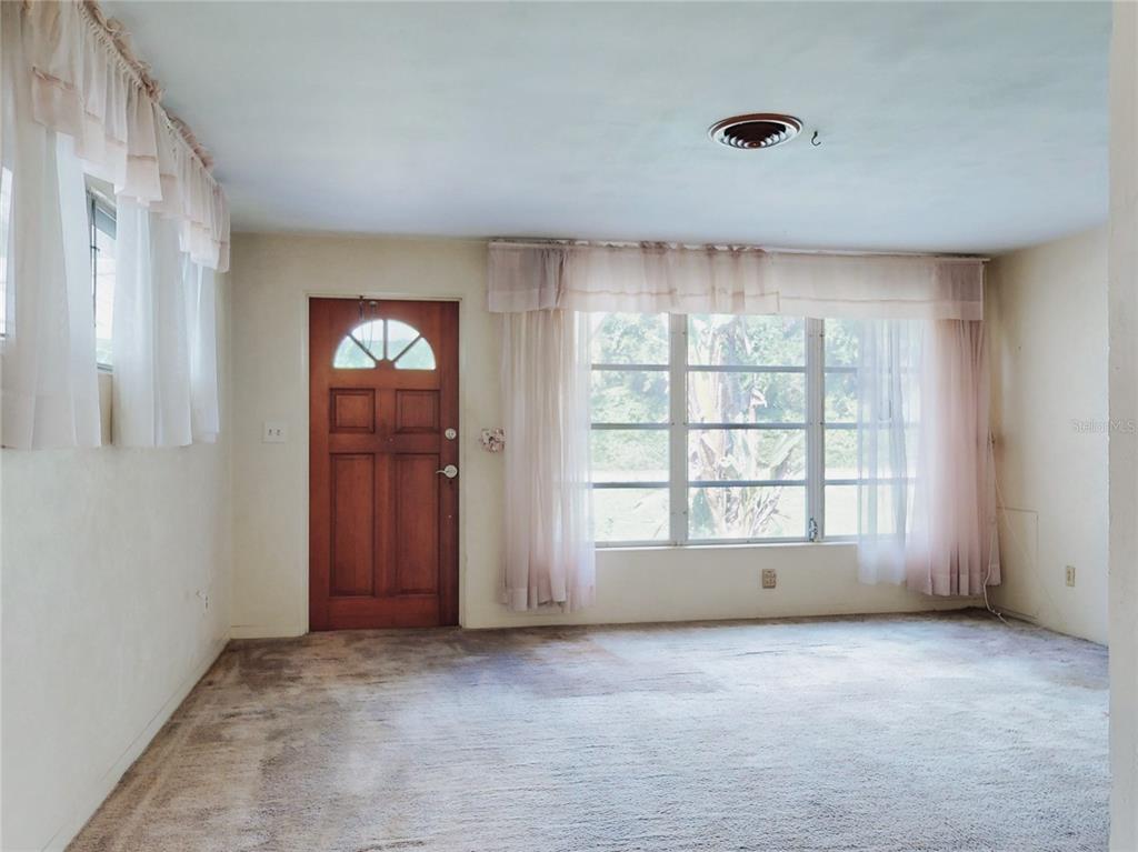 A living room features beige carpeting, a wooden front door, and large windows with curtains — 1307 TURNBULL STREET, NEW SMYRNA BEACH, FL