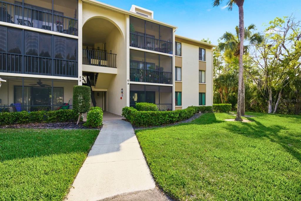 A concrete walkway leads to the entrance of a multi-story apartment building with screened balconies — 3134 LAKE PINE WAY UNIT H1, TARPON SPRINGS, FL