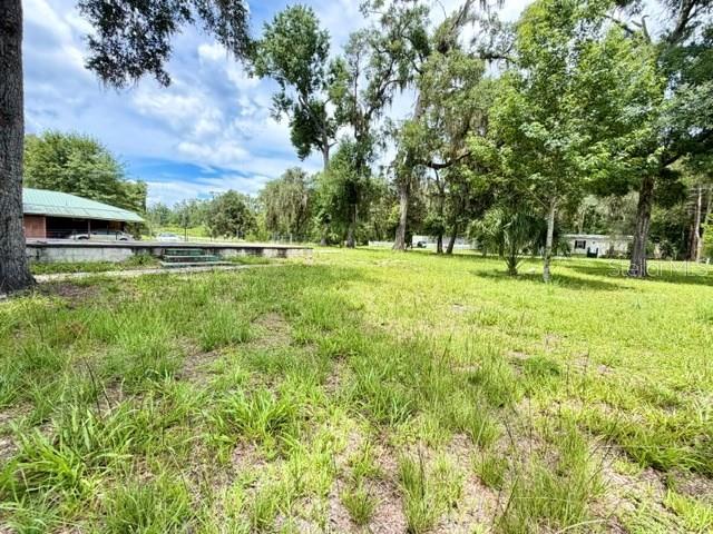 A grassy yard leads toward a house with a covered porch and surrounding trees — 9749 FLORIDA STREET, FANNING SPRINGS, FL