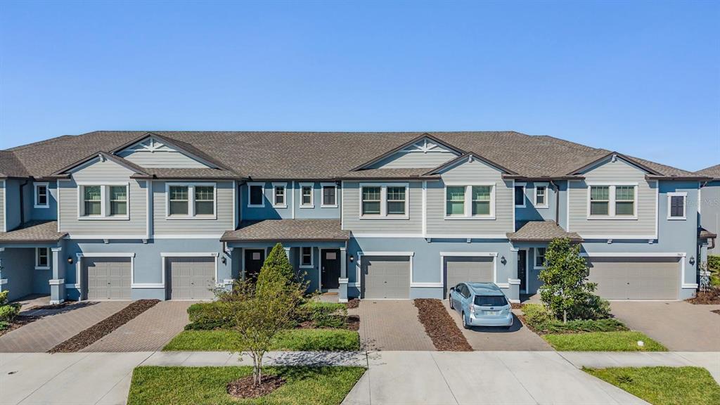 A row of multi-story townhomes with grey siding, shingled roofs, and attached garages — 9661 ASHWORTH PLACE, LAND O LAKES, FL