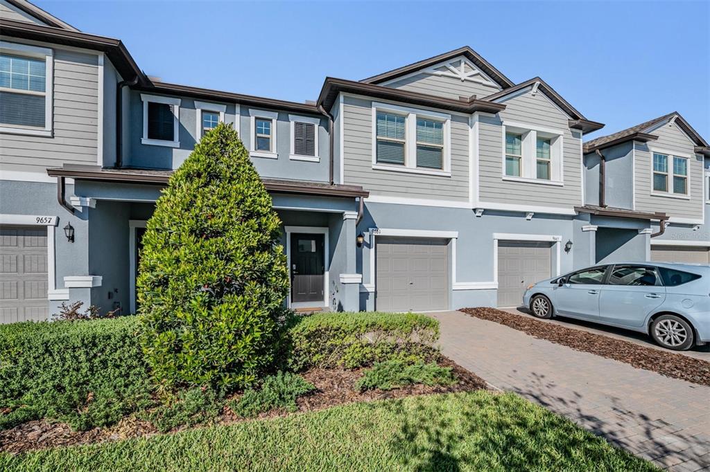 A row of two-story townhomes with gray siding, attached garages, and a landscaped front yard — 9661 ASHWORTH PLACE, LAND O LAKES, FL