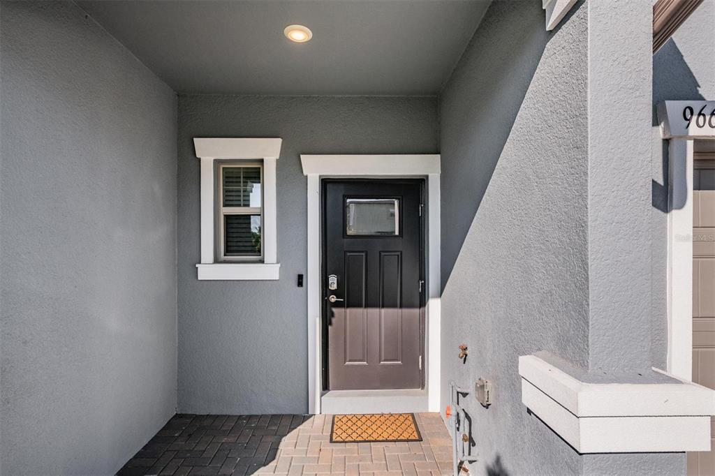 A gray exterior entryway features a dark front door, a window, and a paved floor — 9661 ASHWORTH PLACE, LAND O LAKES, FL