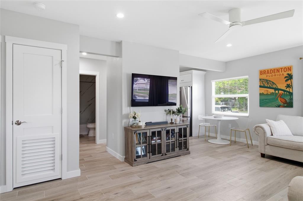 A living room features light wood-look flooring, a wall-mounted television, and a Bradenton wall poster — 1902 SAINT GEORGE DRIVE, BRADENTON, FL