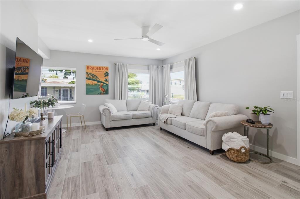 A living room features light gray walls, wood-look tile flooring, two sofas, and a television — 1902 SAINT GEORGE DRIVE, BRADENTON, FL