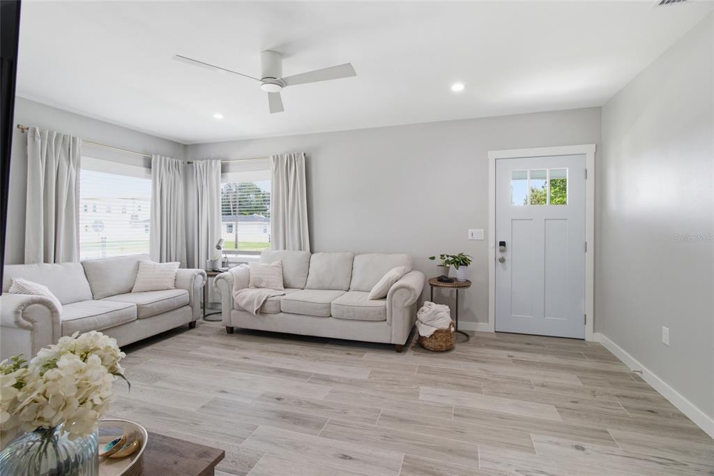 A living room features light gray walls, wood-look tile flooring, two sofas, and a front door — 1902 SAINT GEORGE DRIVE, BRADENTON, FL