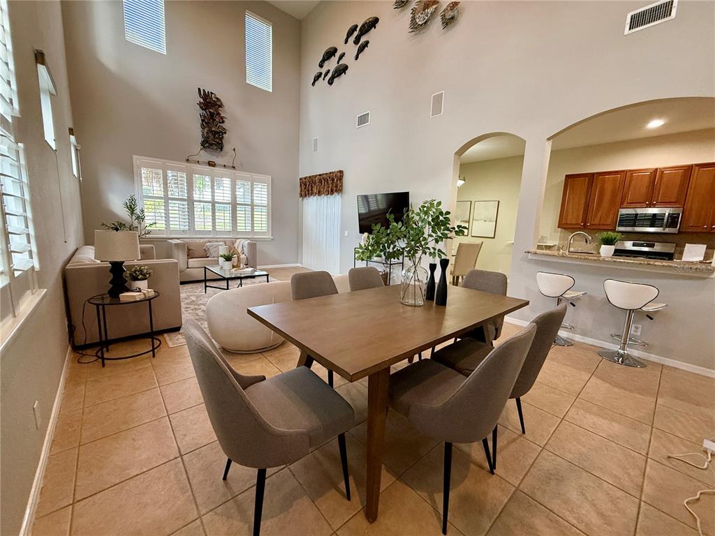 A dining area with a large table and chairs opens into a high-ceilinged living room — 445 NOBLE FAIRE DRIVE, SUN CITY CENTER, FL