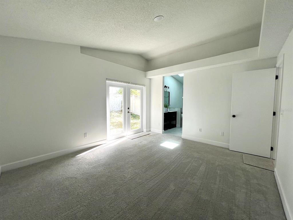 A bedroom with gray carpet, white walls, a vaulted ceiling, and French doors leading outside — 1716 CHATHAM CIRCLE, APOPKA, FL