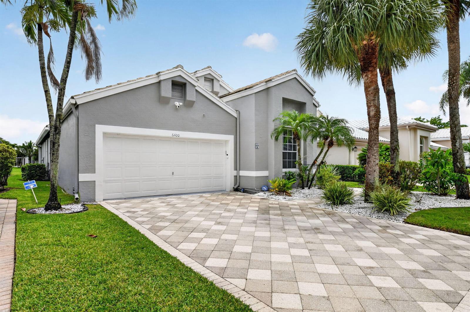 A gray single-story house with a paved driveway, a two-car garage, and palm trees — 6400 Three Lakes Lane, Boynton Beach FL 33437, BOYNTON BEACH, FL