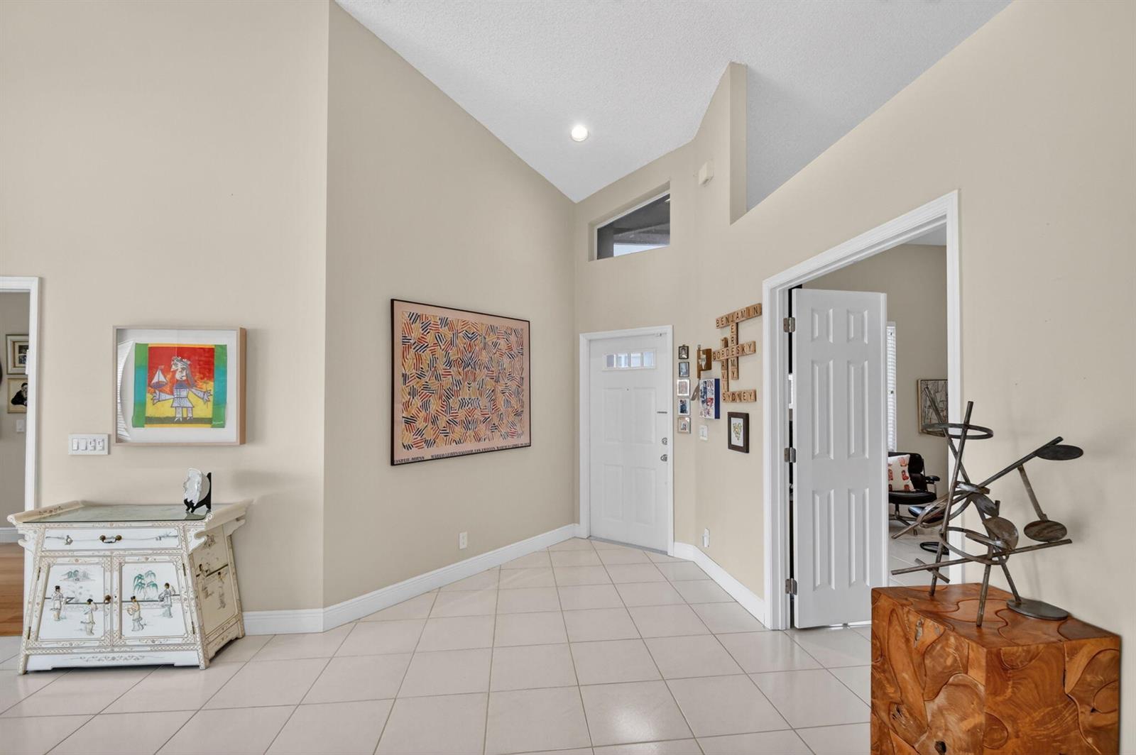 A bright entryway features vaulted ceilings, tile flooring, a white front door, and wall art — 6400 Three Lakes Lane, Boynton Beach FL 33437, BOYNTON BEACH, FL