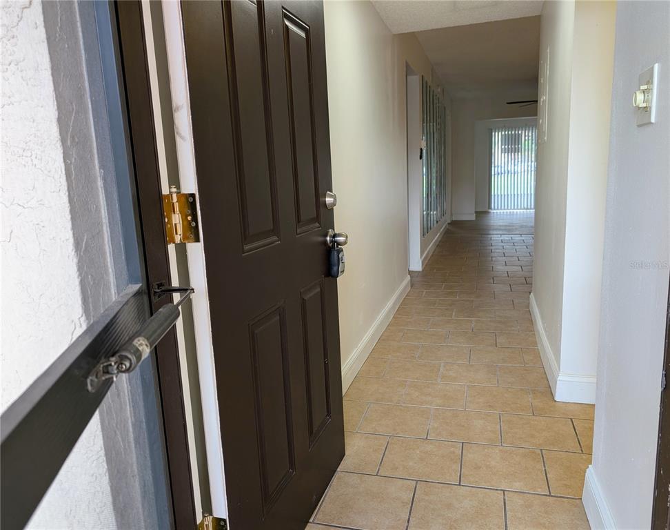An open brown front door reveals a tiled hallway leading to a window with blinds — 4127 HERON WAY UNIT E-111, BRADENTON, FL