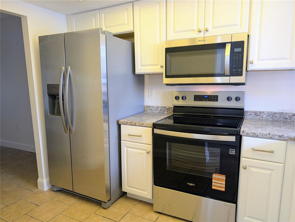 A kitchen features stainless steel appliances, white cabinets, and speckled granite countertops — 4127 HERON WAY UNIT E-111, BRADENTON, FL