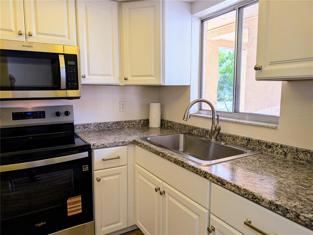 A kitchen features white cabinets, granite countertops, a stainless steel sink, and Whirlpool appliances — 4127 HERON WAY UNIT E-111, BRADENTON, FL