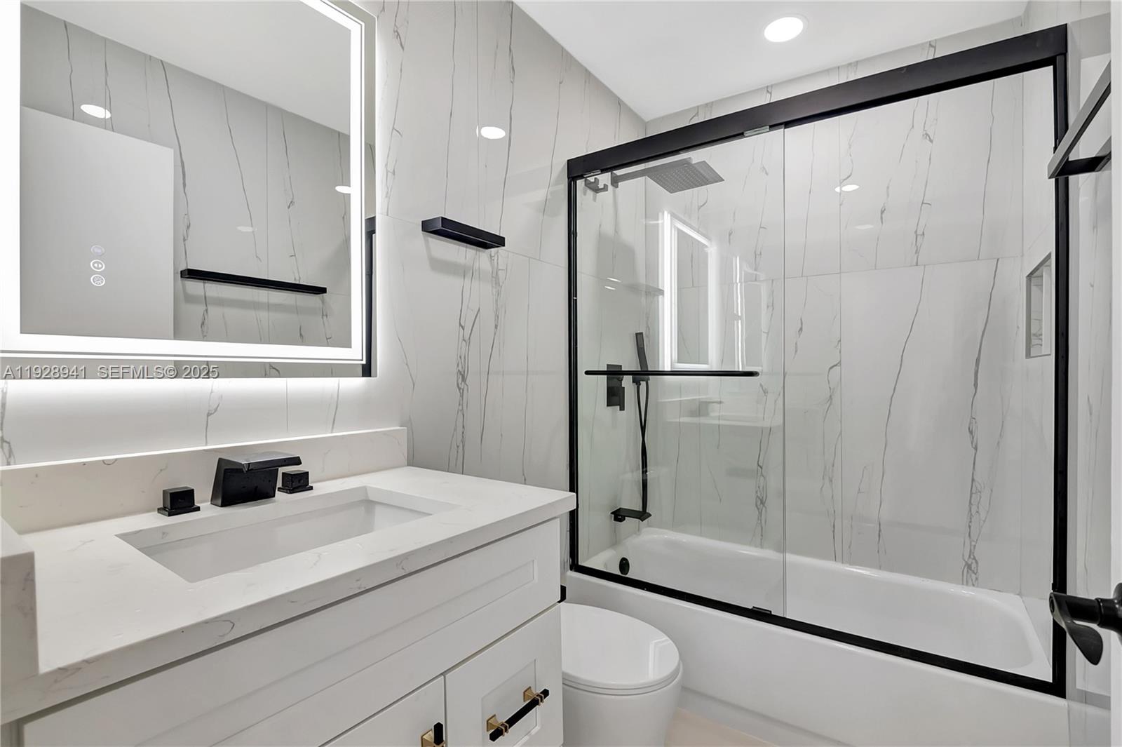 A modern bathroom features a white vanity, marble-look tile walls, and a glass-enclosed shower-tub — 708 Normandy O # 708, Delray Beach FL 33484, DELRAY BEACH, FL