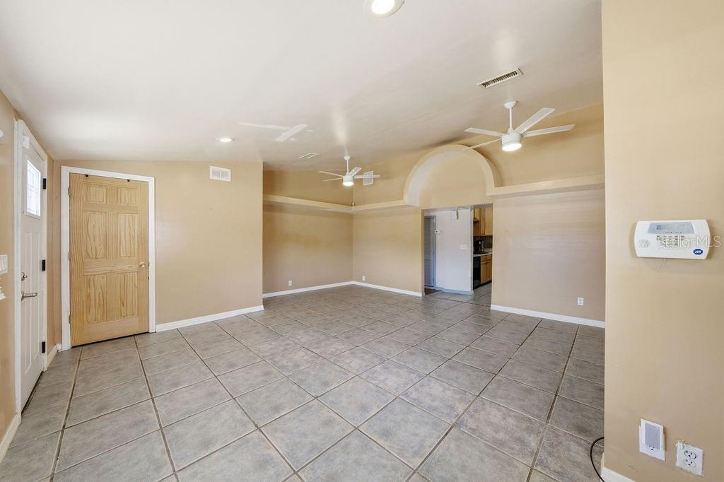 An empty room with beige walls, tile flooring, two ceiling fans, and an arched doorway — 7207 S WEST SHORE BOULEVARD, TAMPA, FL